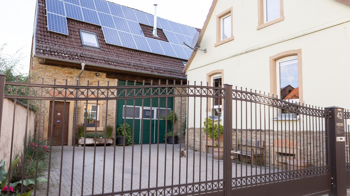 Torzufahrt mit schmiedeeisernem Tor zum Hauptsitz in Dielheim Balzfeld, im Hintergrund ein Gebäude mit Solaranlage auf dem Dach