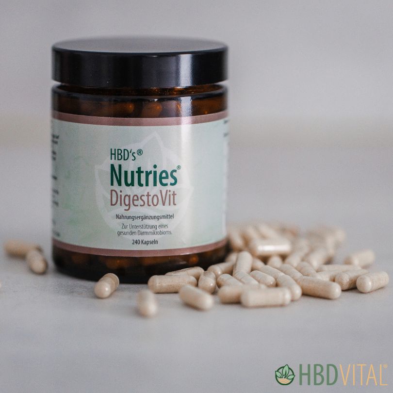 Braunes Glas mit der Aufschrift „HBD’s Nutries® DigestoVit“, einem Nahrungsergänzungsmittel zur Unterstützung eines gesunden Darmmikrobioms. Im Vordergrund liegen geöffnete weiße Kapseln, die Produktverpackung und die Kapseln sind scharf dargestellt.